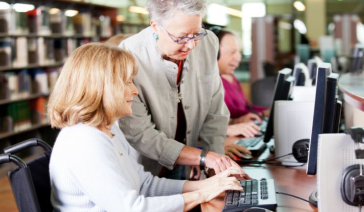 Senior female training with an instructor, sitting at a computer.