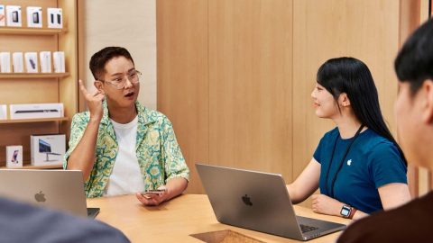 People sitting at a meeting table, using Apple laptops and iPhone accessibility to have a discussion.